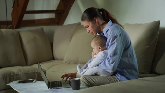 一位幸福的母亲和她刚出生的婴儿的真实照片正在笔记本电脑上观看视频