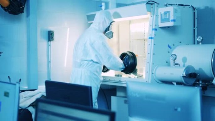 一个穿着防溅服的男人正在实验室里用真空柜工作
