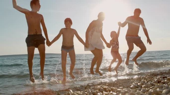超级SLO MO家庭有三个孩子在日落时在海滩上跳跃