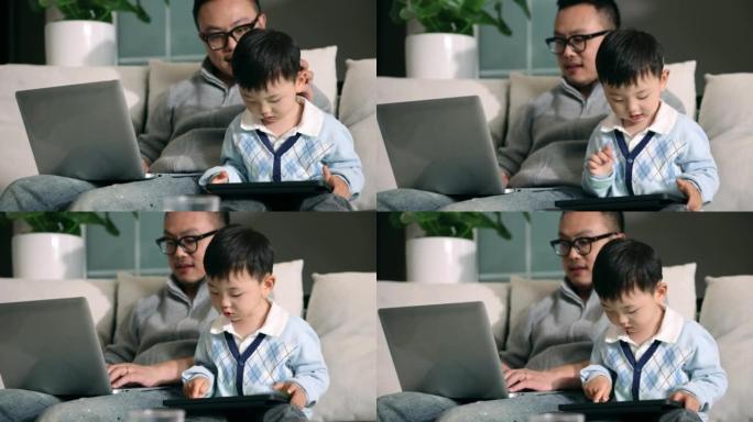 父亲使用笔记本电脑，儿子在沙发上使用平板电脑
