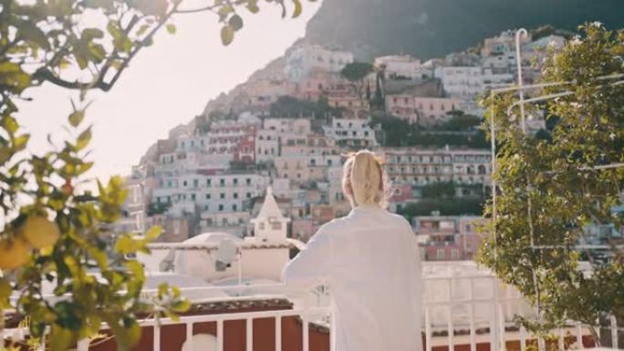 穿着白衬衫的SLO MO女人在度假别墅的阳台上享受早晨的阳光，可以看到波西塔诺的美丽景色