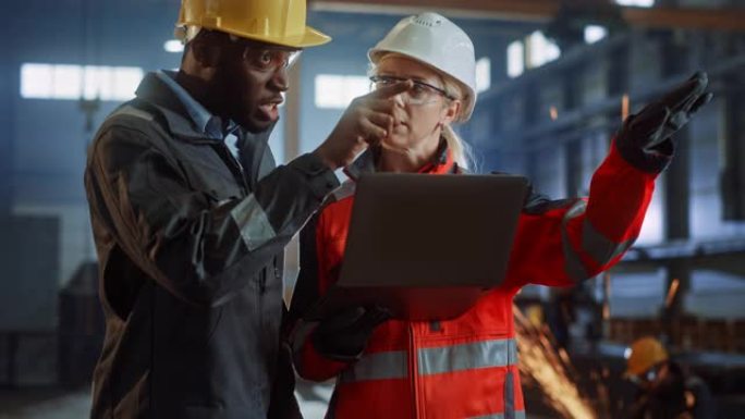 两名重工业工程师站在钢铁金属制造厂，使用数字平板电脑并进行讨论。黑人非裔美国工业专家与女技术员交谈。
