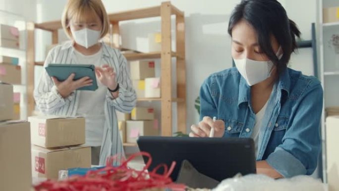 年轻的亚洲女商人戴口罩检查库存产品采购订单，并保存到家庭办公室的平板电脑工作。