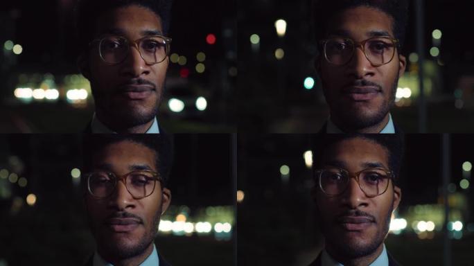 一个英俊时尚的黑人男性的特写镜头，戴着眼镜，晚上站在街上，认真地看着相机。穿着带有Bokeh灯光的西