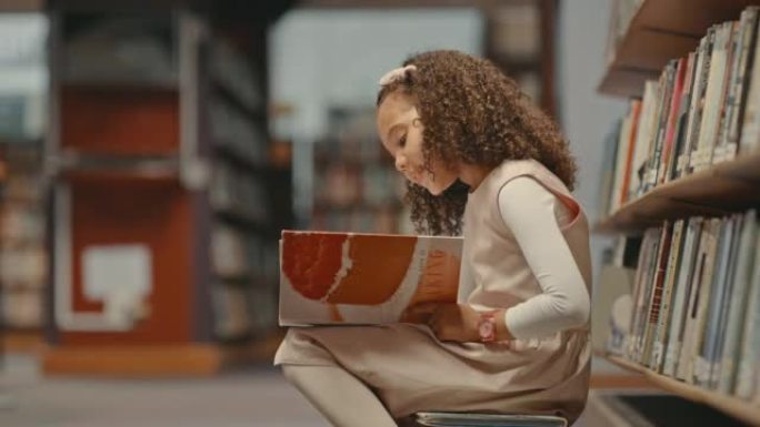 小女孩独自在图书馆。做研究的小孩。可爱的孩子在图书馆做她的学校工作。