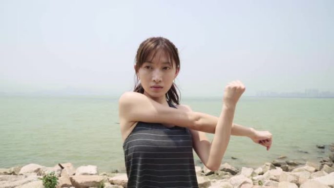 年轻的亚洲妇女在海滩上伸展手臂