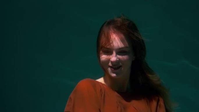 电影特写肖像，美丽的年轻幸福的女人摆姿势，微笑着穿着波西米亚服装潜水水下慢动作。