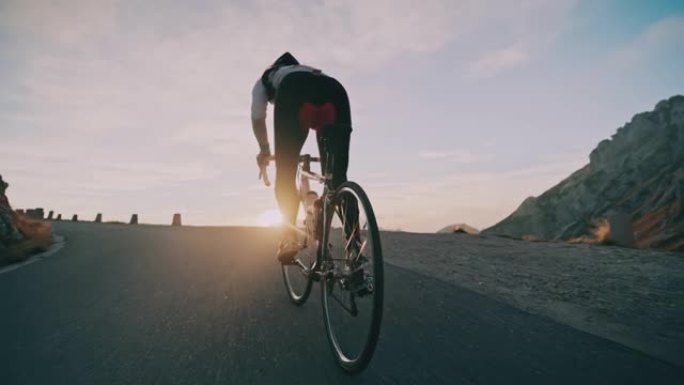 追踪骑自行车的人在日出山上的道路上坡骑自行车
