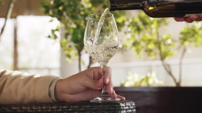 餐厅服务员把瓶子里的白葡萄酒装满玻璃杯特写。酒精饮料在抽象酒吧的透明酒杯中飞溅。植物背景上的风味晚餐
