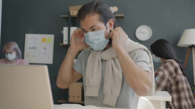 谨慎的员工戴上医用口罩的肖像坐在办公室的办公桌上看着相机
