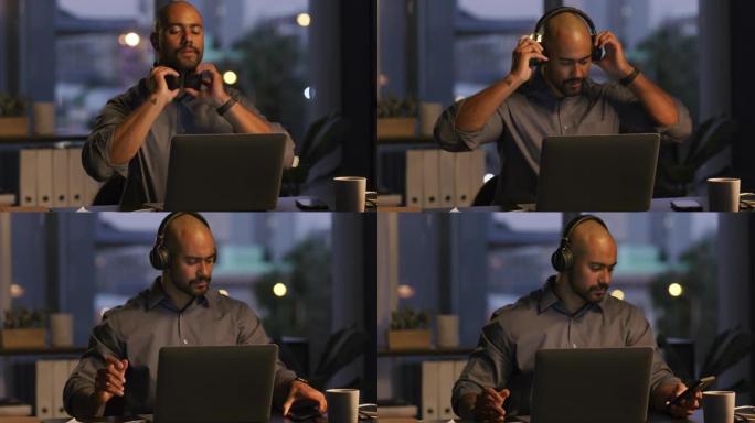 4k视频片段，一个年轻的商人晚上坐在办公室里，戴着耳机使用笔记本电脑