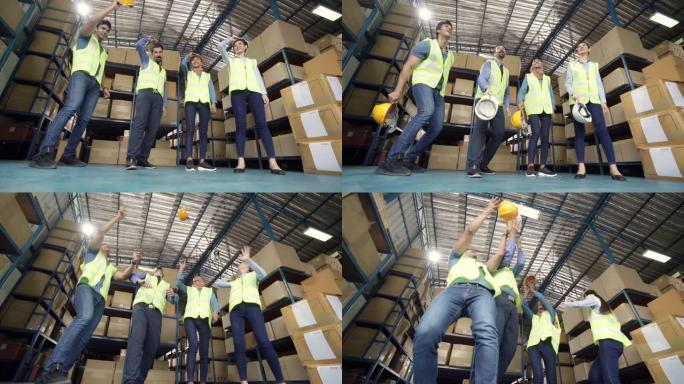 慢动作FHD: 仓库工人和经理的跨种族团队在完成工作后将头盔扔向空中庆祝。用于商业仓库和庆祝概念。