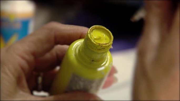 一位高级妇女的手将刷子浸入黄色的油漆罐中。特写。