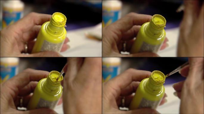一位高级妇女的手将刷子浸入黄色的油漆罐中。特写。