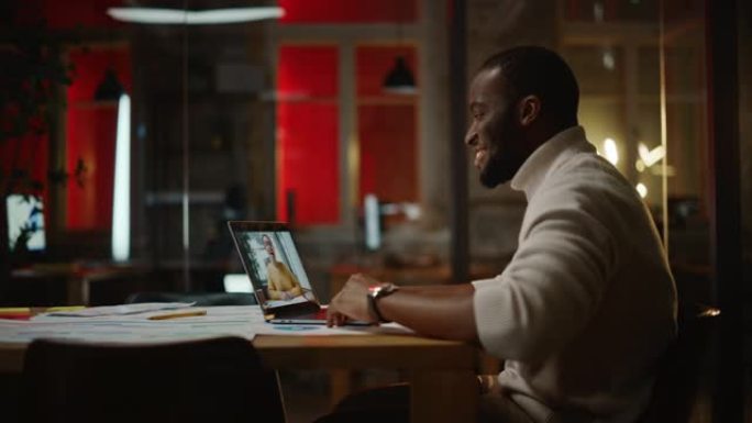 英俊的黑人非洲裔美国项目经理正在创造性的办公环境中使用笔记本电脑进行视频通话。男性专家通过实时摄像机