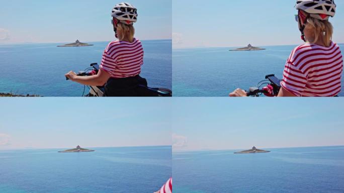 金发碧眼的骑自行车的女人在赫瓦尔岛 (Hvar island) 海岸休息，看着海上的一个小岛，上面有