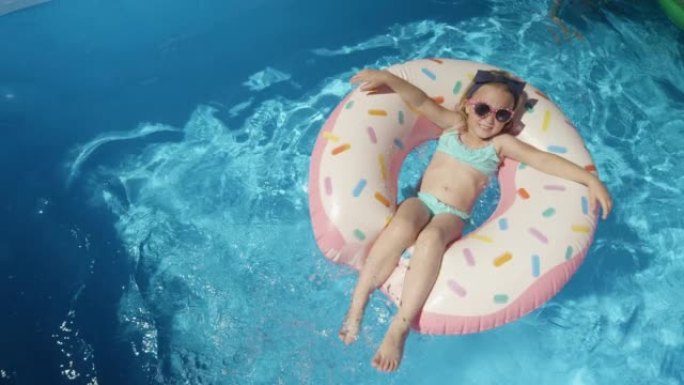 自上而下: 可爱的小女孩，在游泳池的浮动甜甜圈上戴着墨镜