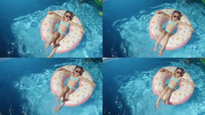 自上而下: 可爱的小女孩，在游泳池的浮动甜甜圈上戴着墨镜
