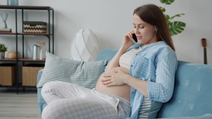 怀孕女孩在手机上聊天在家室内抚摸肚子的慢动作