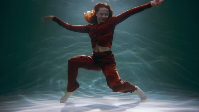幸福概念。电影拍摄的年轻美丽快乐的红发女人在水下慢动作下做有趣的舞蹈动作。