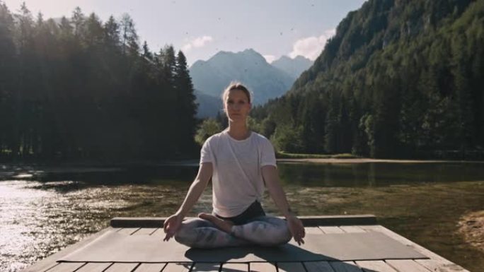 成年女性，金发碧眼，坐在jezersko湖前的木板路上，沉思着她的瑜伽马特