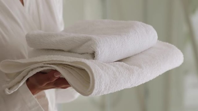 穿着浴袍的女人拿着一堆干净的白色浴巾