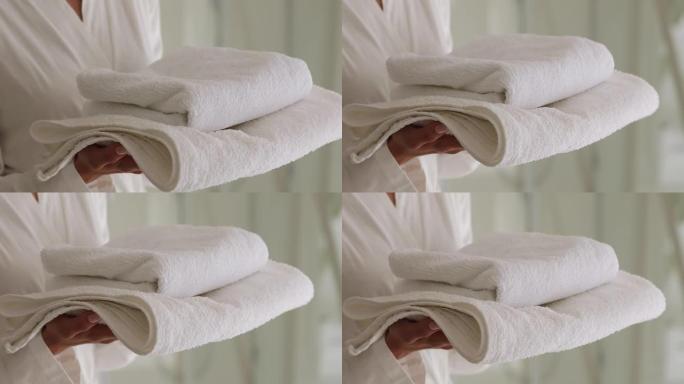 穿着浴袍的女人拿着一堆干净的白色浴巾