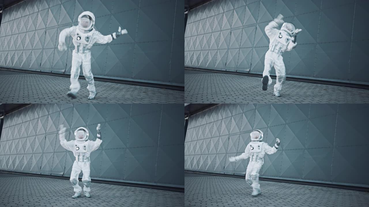 穿着宇航服的英俊男子在金属墙旁边跳舞。宇航员很高兴，并做出了创造性的机器人动作。成功的太空人穿着白色