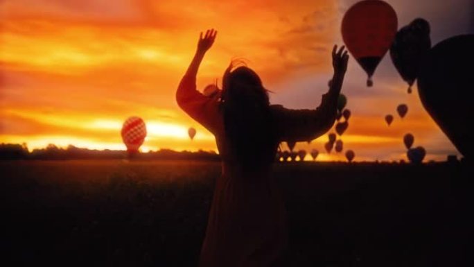 一个无忧无虑的女人在田野里的SLO MO剪影，在黄金时段天空中有热气球