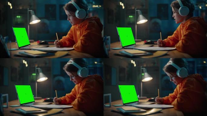 戴着耳机的聪明小男孩在家里绿屏笔记本电脑上参加在线课程。快乐少年在线浏览教育研究，笔记本写作，学习学
