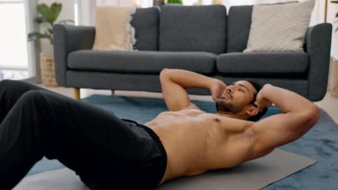 锻炼，锻炼和健身和一个男人做仰卧起坐在他的家的客厅，以健康和健康。一个在房子里锻炼身体的男运动员的激