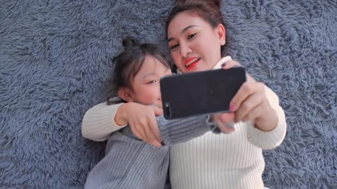 POV: 6岁的亚洲母女在使用智能手机和视频会议技术进行社交距离期间在家中客厅视频通话的视频会议。社