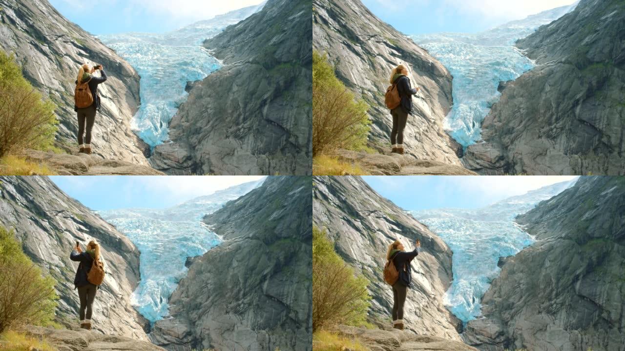 4k视频片段，一个无法识别的女人站着并用手机拍摄Briksdal冰川