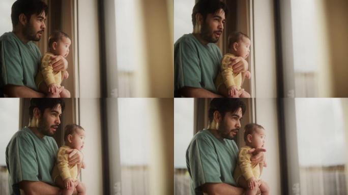 父爱的慢动作肖像: 一个年轻的父亲抱着小婴儿，他透过窗户说话和看着。男人和他可爱的蹒跚学步的孩子一起
