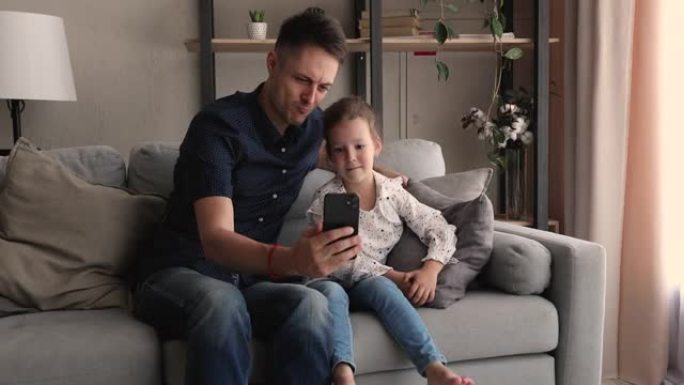 快乐可爱的小女孩与爸爸一起使用有趣的手机应用程序。