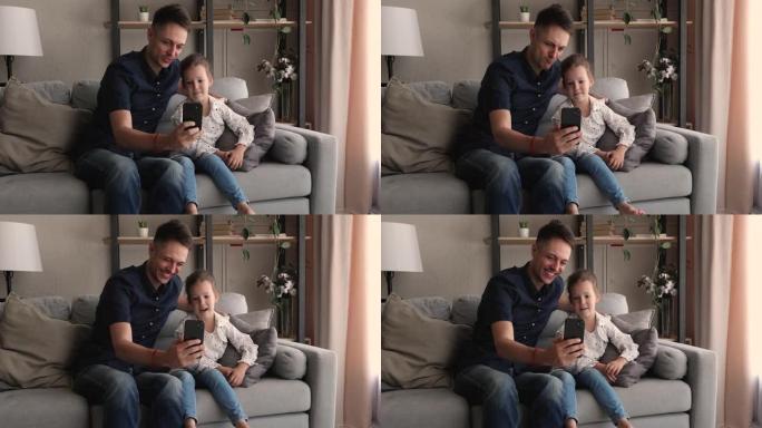 快乐可爱的小女孩与爸爸一起使用有趣的手机应用程序。