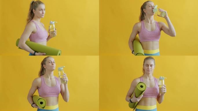 穿着运动服的女孩从瓶子里喝东西，拿着瑜伽垫走在黄色背景上