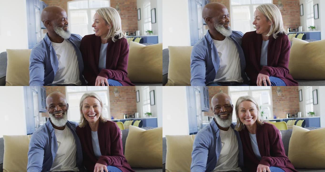 坐在沙发上，拥抱和微笑的客厅里快乐的老年夫妇的肖像