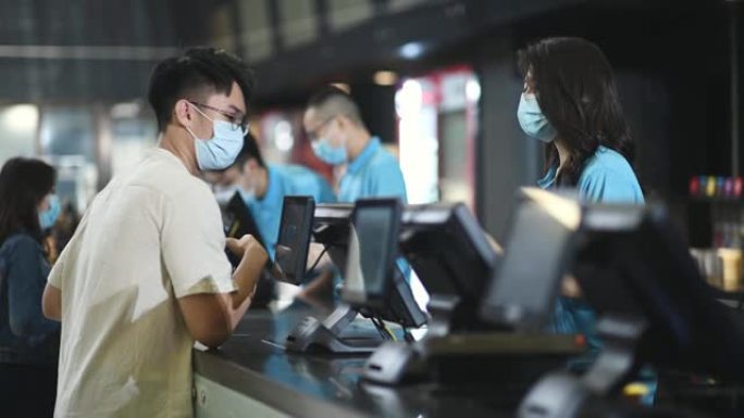 一名戴着面罩的亚裔华人男性顾客在电影院售票处购买电影票