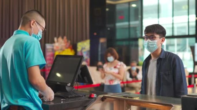 一名戴着口罩的亚洲华裔年轻人在电影院开映前在吧台点了爆米花矿泉水