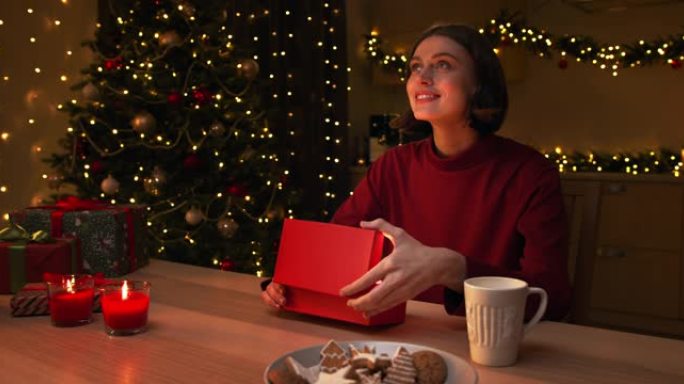 一位穿着红色毛衣的棕色头发的年轻美女打开了一个红色礼品盒，其中的魔光照亮了她的脸