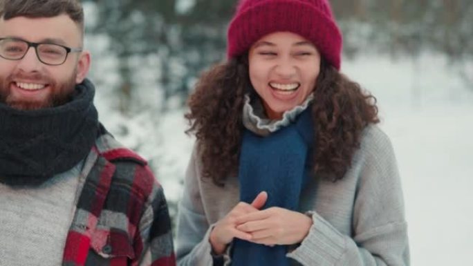 快乐的多民族有趣的年轻朋友微笑，一起笑着穿着温暖的冬装在白雪皑皑的森林慢动作。