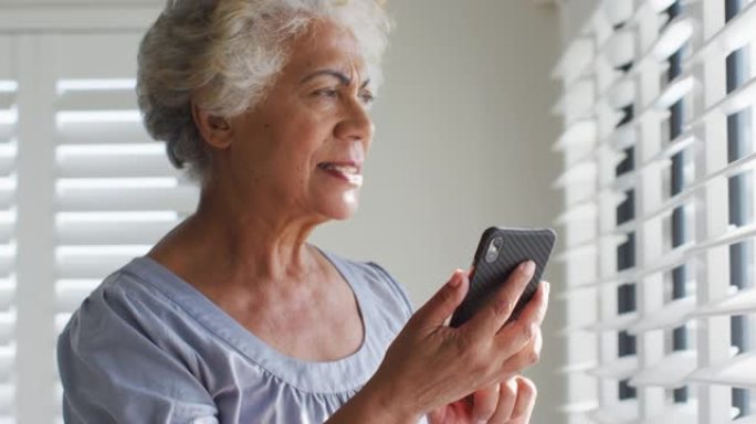 非裔美国高级女性使用智能手机，在家里看着窗外