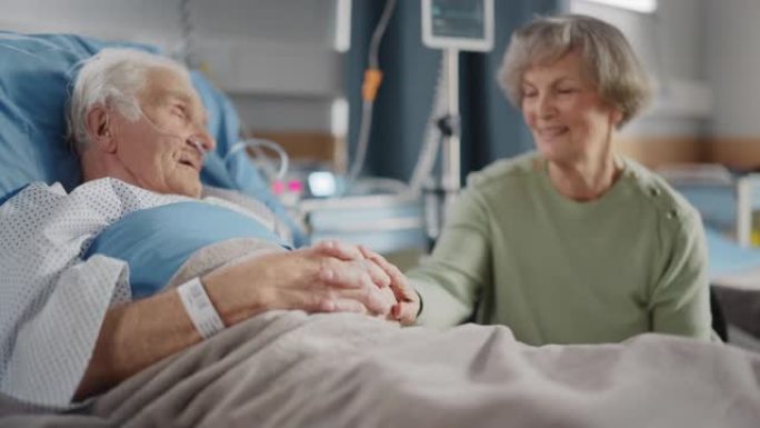 医院病房: 老人躺在床上休息，他有爱心的美丽妻子来访，支持他坐在旁边，手牵着手，幸福的夫妻在一起聊天