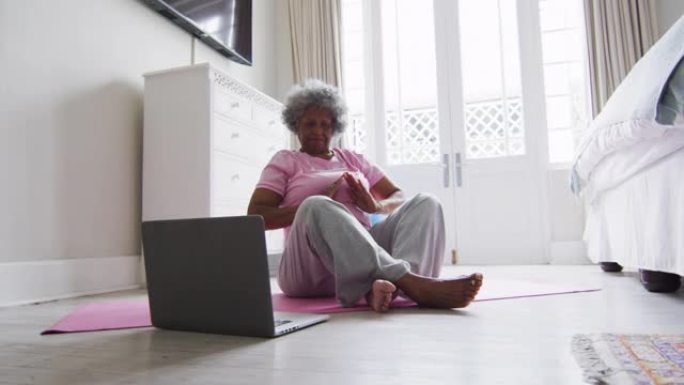 资深非裔美国妇女在家里看笔记本电脑时练习瑜伽