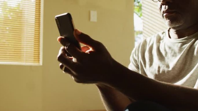 体贴的非洲裔美国老人坐在家里晒太阳，使用智能手机