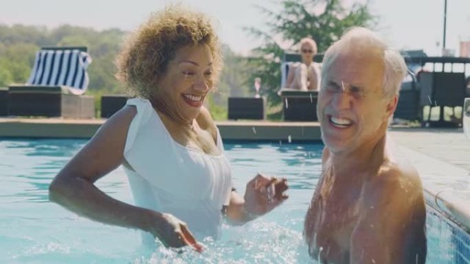 退休的高级夫妇暑假在游泳池里放松，互相泼水