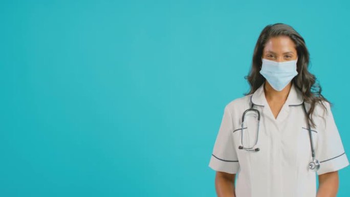 穿着制服戴着口罩的女护士肖像站在蓝色工作室背景前