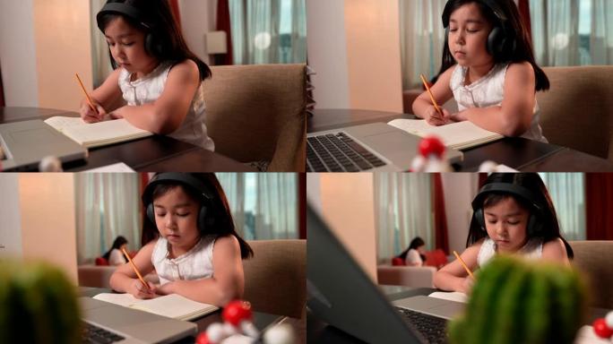 亚洲女孩在网上学习期间通过笔记本电脑和耳机做笔记，笔记本电脑在前台。社交距离，儿童教育，自学，电子学