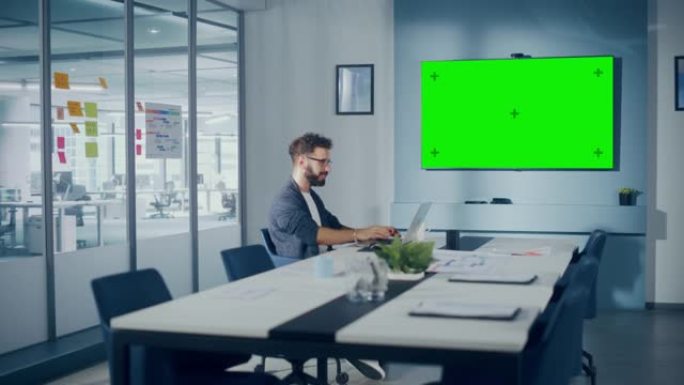 办公室会议室: 在笔记本电脑上工作的英俊的西班牙裔专家与绿屏Choma Key Wall电视互动。在